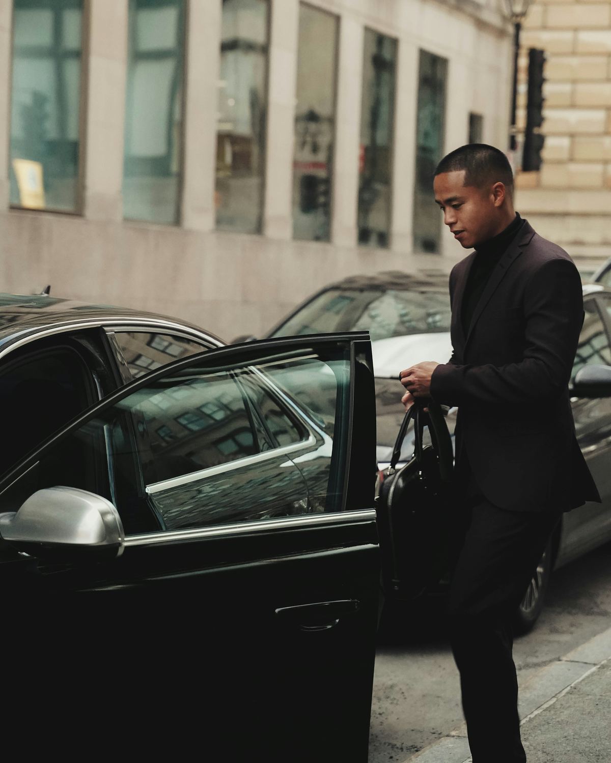 A chauffeur holding the car door open on a city street.