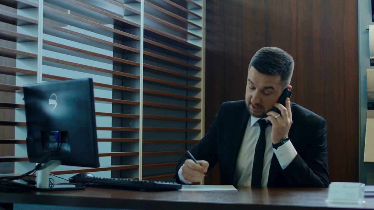 A man on the phone at his desk, taking notes as he organises a request.