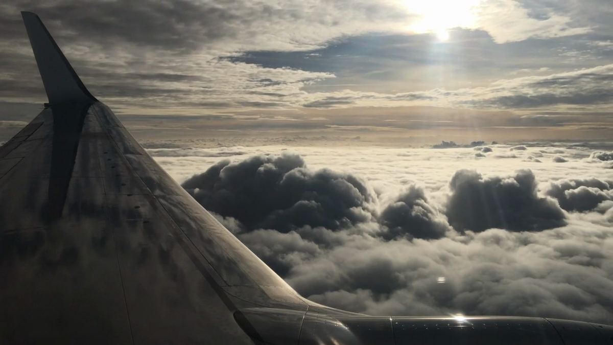 An aircraft wing above a sea of clouds, sunlight breaking through.